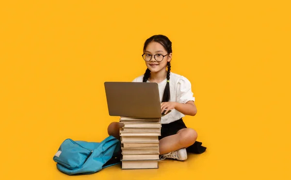 Ázsiai kislány csinál házi feladatot a laptopon sárga háttér — Stock Fotó
