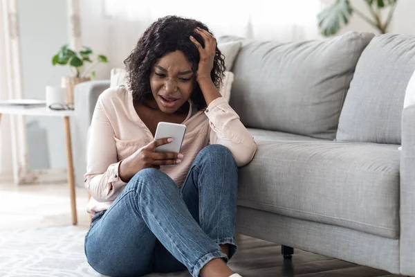 Malas noticias. Molesto mujer africana conmocionada lectura mensaje en el teléfono inteligente en casa —  Fotos de Stock
