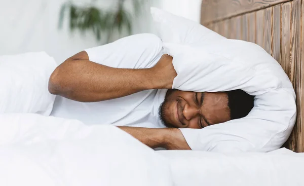 Нарушенный человек, закрывающий уши подушкой, страдающей от бессонницы в помещении — стоковое фото