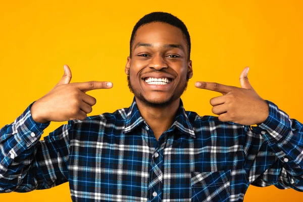 Чорний хлопець вказує пальці на його білі зуби, студійний знімок — стокове фото