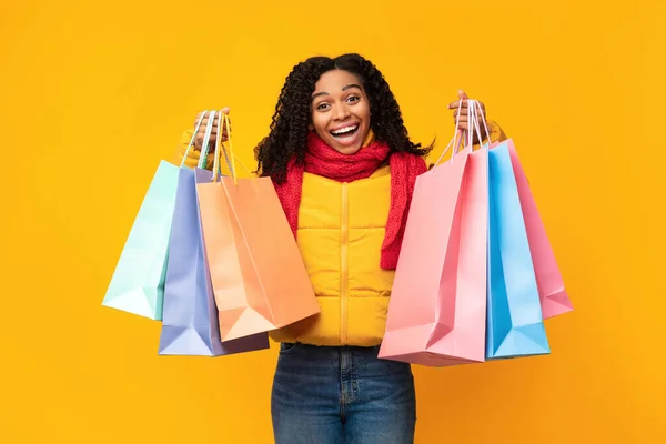 Chica emocionada con bolsas de compras posando con chaqueta, fondo amarillo —  Fotos de Stock