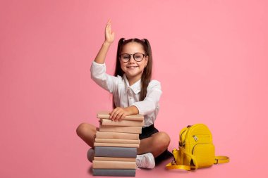Zeki bir öğrenci. Sırt çantası ve kitap yığınıyla gülümseyen kız cevabı biliyor ve elini kaldırıyor.