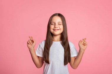 Gözleri kapalı, parmakları çapraz gülümseyen bir çocuk dilek tutar.