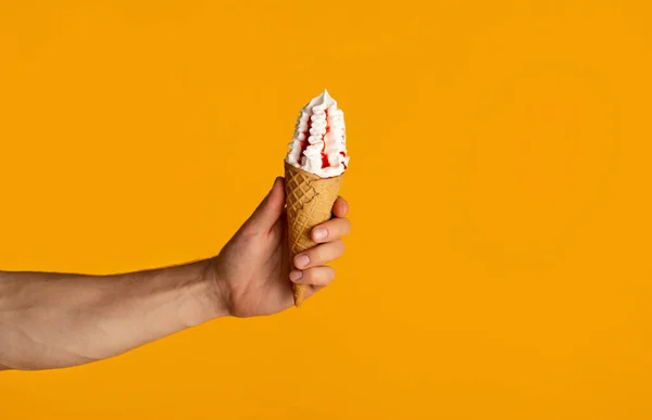 Cropped view of millennial guy holding yummy ice cream in waffle cone over orange background, closeup — Stock Photo, Image