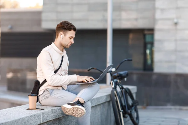 Biuro online outdoor. Zajęty człowiek pracujący na laptopie ze słuchawkami bezprzewodowymi — Zdjęcie stockowe