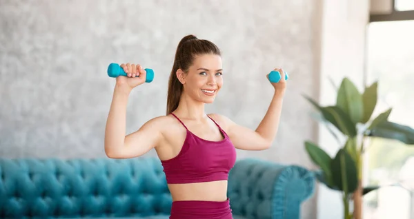 Hemmaträning. Atletisk ung flicka i sportkläder träning med hantlar inomhus — Stockfoto