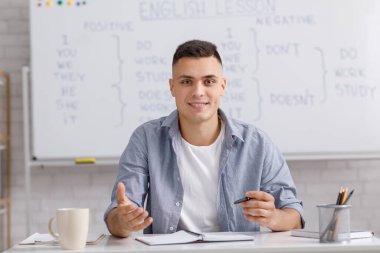 Web kamerasıyla konuşan çevrimiçi öğretmen, ofiste masada oturuyor ve İngilizce kurallarını anlatıyor.