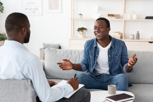 Udana terapia. Radosny czarny mężczyzna rozmawia z psychologiem w swoim biurze — Zdjęcie stockowe