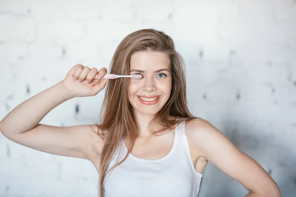 Cuidados dentários. Menina atraente com sorriso radiante segurando escova de dentes dentro de casa — Fotografia de Stock