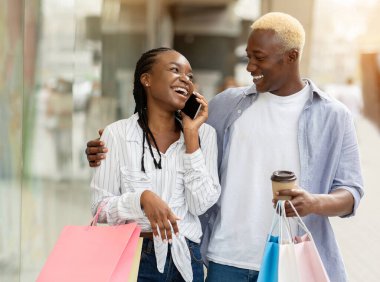 Hafta sonu ve alışveriş. Akıllı telefonları ve ellerinde alışveriş çantaları olan Afrikalı Amerikalı bir çiftin portresi.