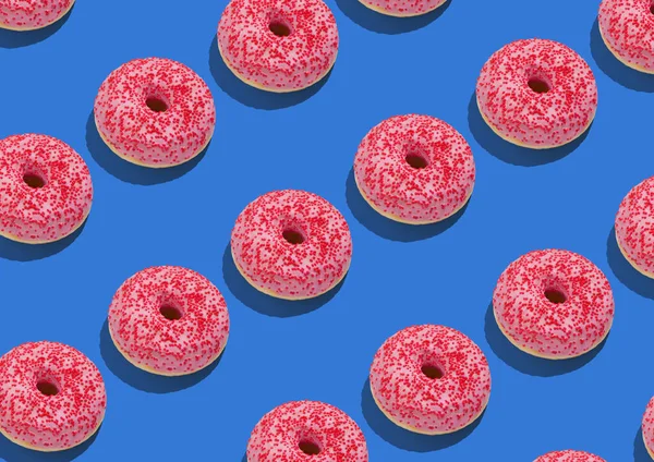 Pembe buzlu lezzetli çörekler ve mavi arka planda kırmızı serpiştirmeler. — Stok fotoğraf