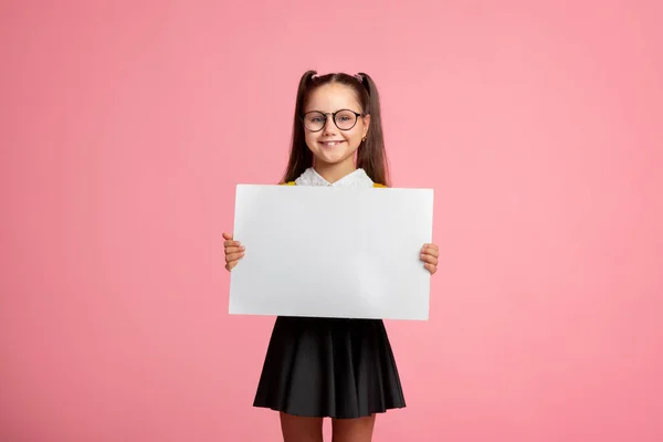 Vidám iskolás lány egyenruhában és szemüvegben tartja jel üres hely — Stock Fotó