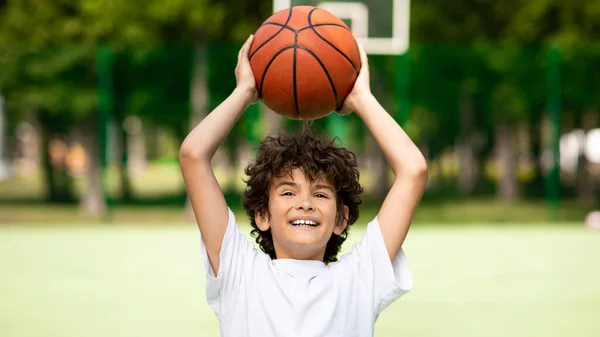 Potret anak laki-laki keriting yang sportif melempar bola basket — Stok Foto