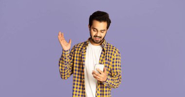 Heyecanlı Hintli adam menekşe arka planında elinde akıllı telefona bakıyor.