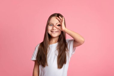 Her şey yolunda. Gülümseyen çocuk işaret dilini kullanırken parmaklarının arasından bakıyor.