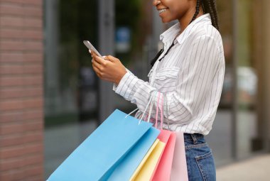 Dükkanlardan en iyi teklif. Çantalı mutlu Afro-Amerikan kadın mağazadan yorum yapıyor.