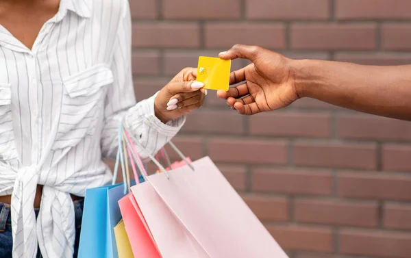 Girl shopper with colored bags gives credit card to seller