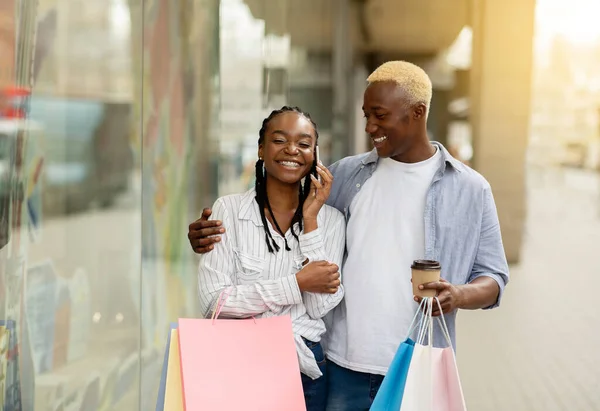 Shoppers uiten blijdschap door telefonisch te praten. glimlachen Afrikaans amerikaans paar met gekleurde zakken — Stockfoto