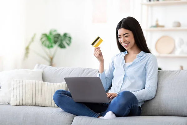 Evde bilgisayar ve kredi kartı kullanan neşeli Asyalı kadın internetten alışveriş yapıyor. — Stok fotoğraf