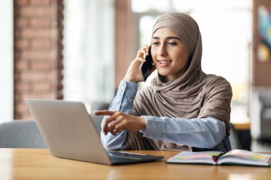 Türbanlı Arap kadın kafede telefonla konuşuyor.