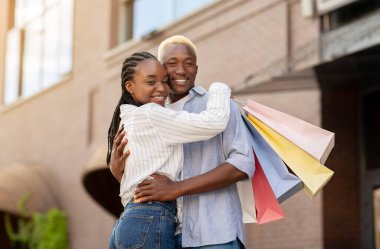 Hafta sonları ve alışveriş merkezinde alışveriş. Renkli çantalı mutlu adam ve kadın sarılır