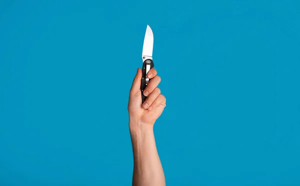Jeune homme méconnaissable tenant un couteau de poche sur fond bleu, gros plan de la main — Photo