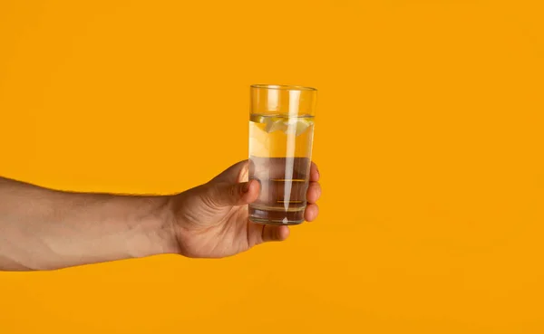Junger Mann mit Glas klaren Trinkwassers auf orangefarbenem Hintergrund, Nahaufnahme — Stockfoto