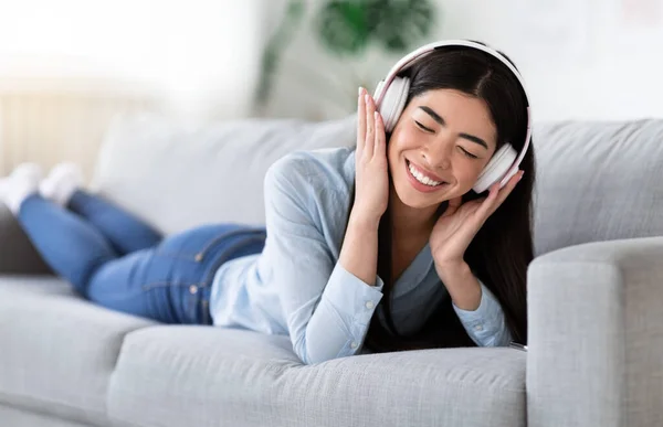 Hora de relajarse. alegre asiático chica en auriculares escuchar música en sofá — Foto de Stock