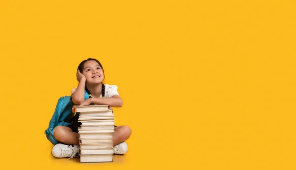 Chinese School Girl Sitting At Books Stack On Yellow Background