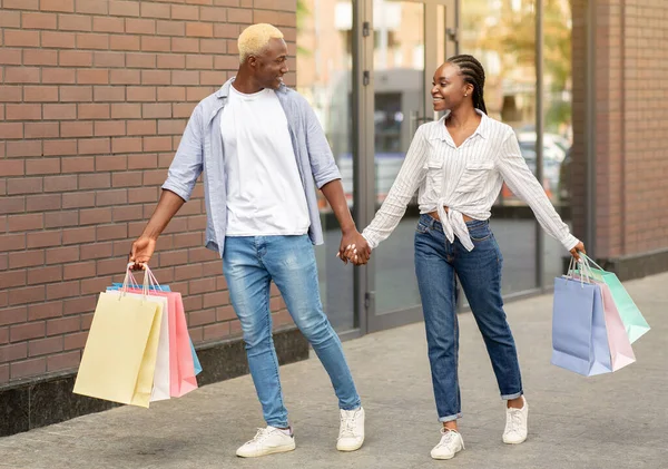 Gelukkig Afrikaans Amerikaans paar met boodschappentassen wandelen in de buurt van winkelcentrum — Stockfoto