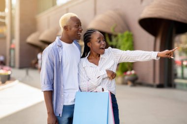 Yeni kıyafet koleksiyonu. Alışveriş poşetleriyle hayret verici bir adam ve kız vitrinde görünüyor.