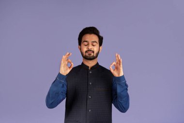 Huzurlu Hintli adam meditasyon yapıyor ve eflatun arka planında yoga yapıyor.