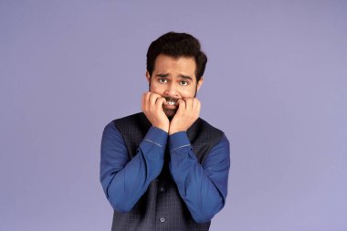 Korkmuş Hintli adam, leylak arkaplanı yüzünden panik içinde tırnaklarını yiyor.