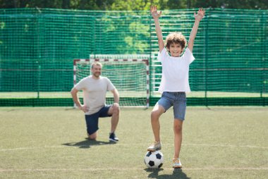 Futbol sahasında futbol topuyla poz veren küçük çocuk.