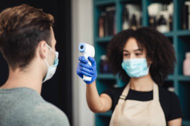 Kadın usta, berber dükkanındaki genç adamın vücut ısısını ölçüyor.