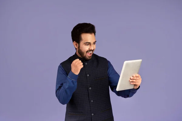 Hombre indio emocionado con la tableta de la computadora haciendo SÍ gesto sobre fondo violeta —  Fotos de Stock