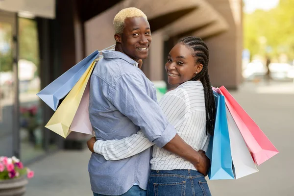 Gelukkig jong Afrikaans Amerikaans paar wandelen in de stad na het winkelen met kleurrijke tassen — Stockfoto