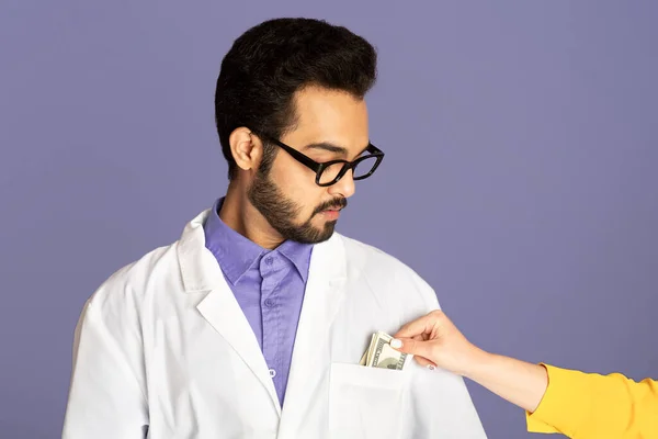 Corrupción en la medicina. Paciente poniendo dinero en el bolsillo de los médicos indios sobre fondo lila — Foto de Stock