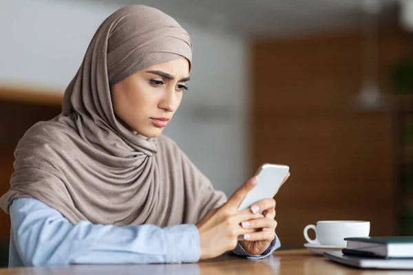 Trauriges muslimisches Mädchen mit Handy, Café-Innenraum — Stockfoto