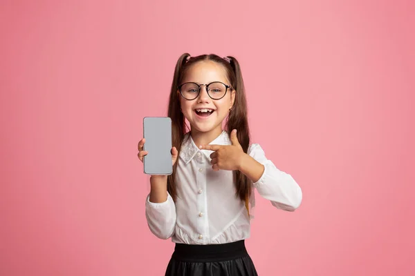 Happy schoolmeisje in bril met open mond toont duim omhoog en smartphone met leeg scherm — Stockfoto