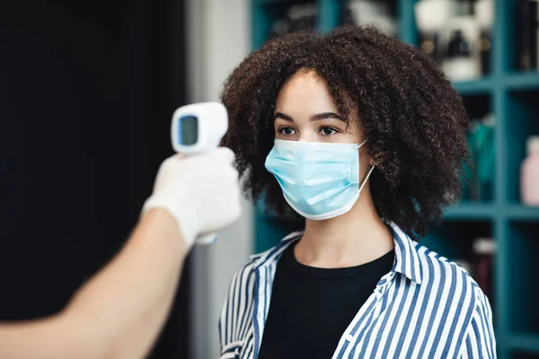 Jovem mulher negra em máscara protetora obtendo temperatura check-up no salão — Fotografia de Stock
