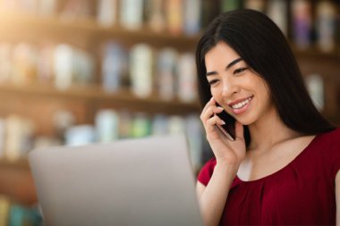 Cafe 'de dizüstü bilgisayarda çalışırken cep telefonuyla konuşan Asyalı girişimci.