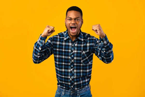 Känslomässig afrikansk man skriker högt skakar knytnävar över gul bakgrund — Stockfoto