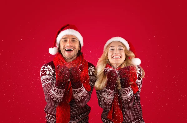 En Navidad. feliz millennial chico y su novia soplando nieve sobre rojo fondo — Foto de Stock