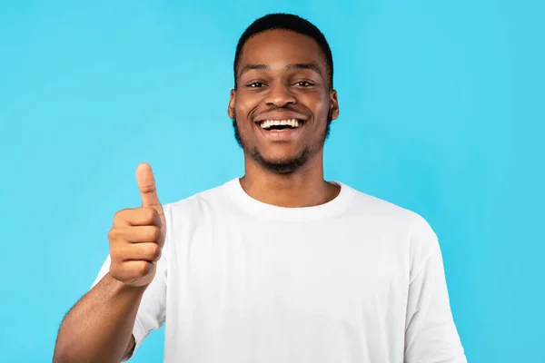 Fröhlicher Afroamerikaner gestikuliert mit dem Daumen nach oben und posiert vor blauem Hintergrund — Stockfoto