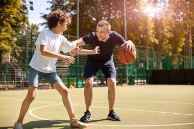 Olgun bir adam çocuğa basketbol oynamayı öğretiyor.