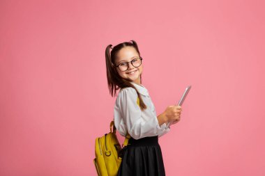 Çocuk çalışmak için aletler kullanıyor. Sırt çantalı neşeli liseli kız dijital tablet taşıyor