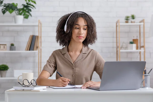 Afrikaans-Amerikaanse millennial student in hoofdtelefoon zitten aan het bureau, kijken webinar en het maken van aantekeningen — Stockfoto