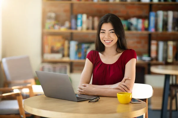 Freelancer asiatisch mädchen lächelnd bei camera während arbeit auf laptop im cafe — Stockfoto