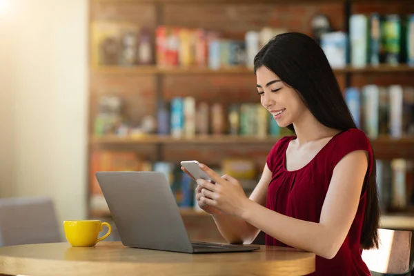 Fröhliche asiatische Unternehmerin nutzt Smartphone bei der Arbeit mit Laptop im Café — Stockfoto